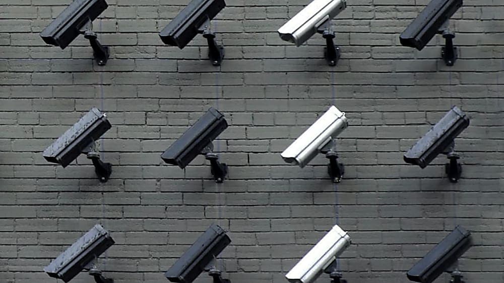 schwarze und silberne Sicherheitskameras an grauer Backsteinwand, die alle in eine Richtung zeigen.